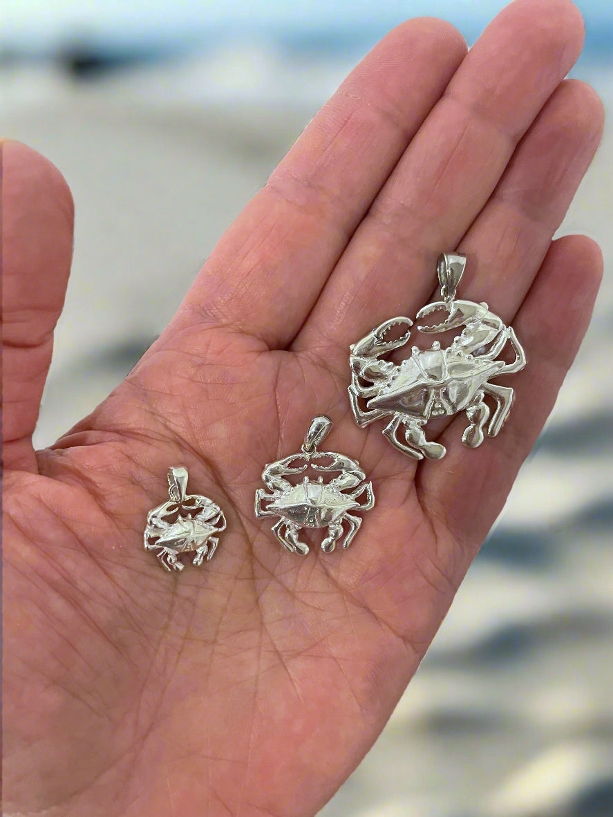 Three silver crab pendants on a hand with a blurred beach background