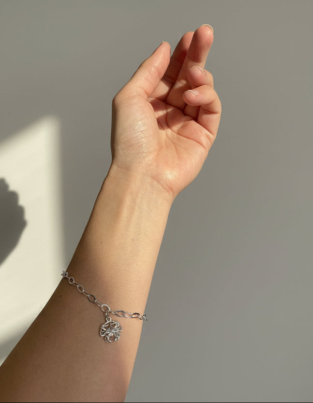Hand wearing a silver bracelet with a starfish charm against a neutral background