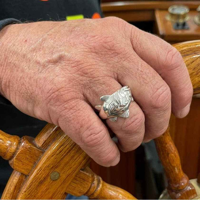 man wearing silver fish ring placing his hand on boat wheel