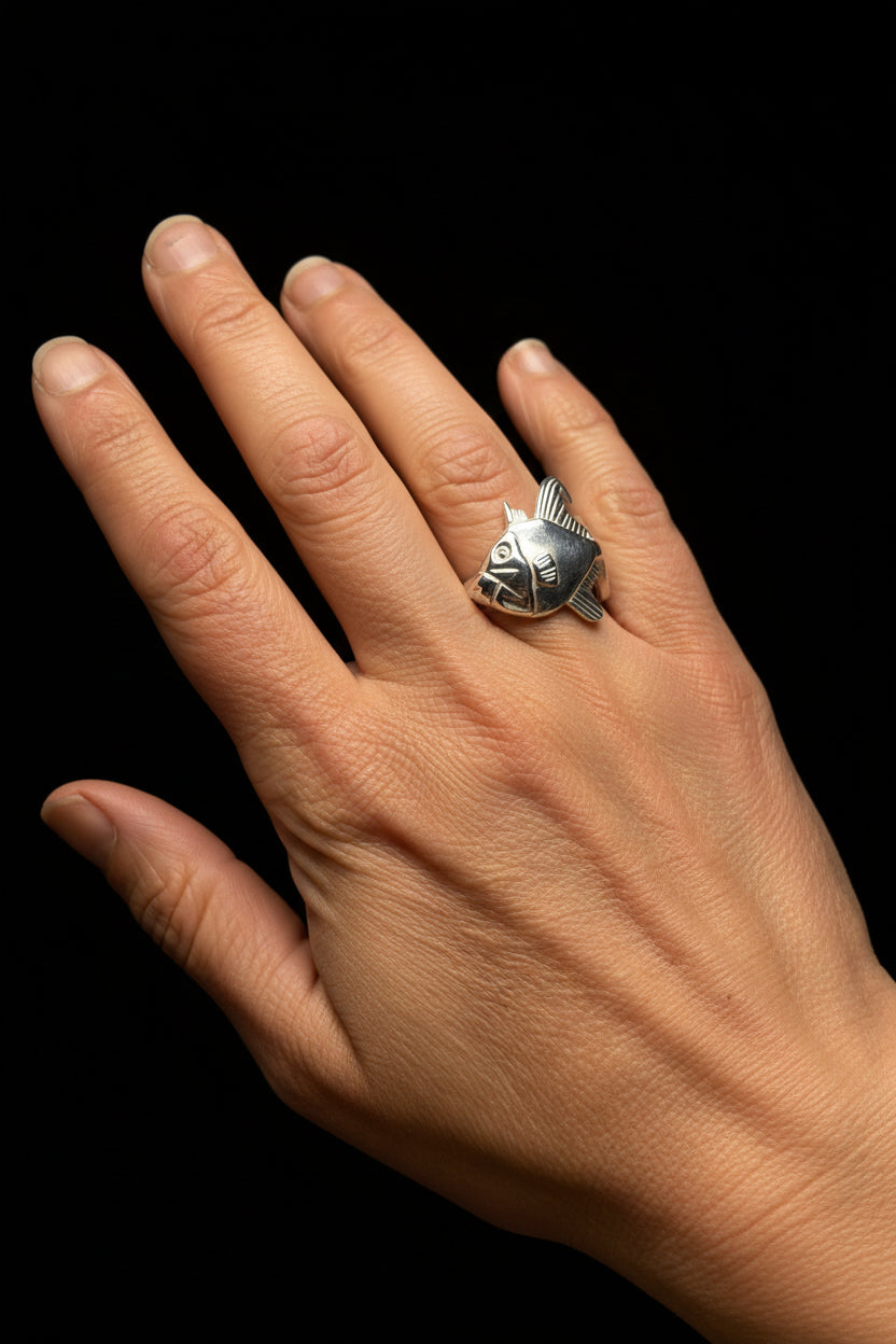 A silver ring with triggerfish design worn on a person's ring finger, shown against a plain light gray background.