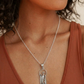 Silver necklace with a pendant worn by a person in a brown top.