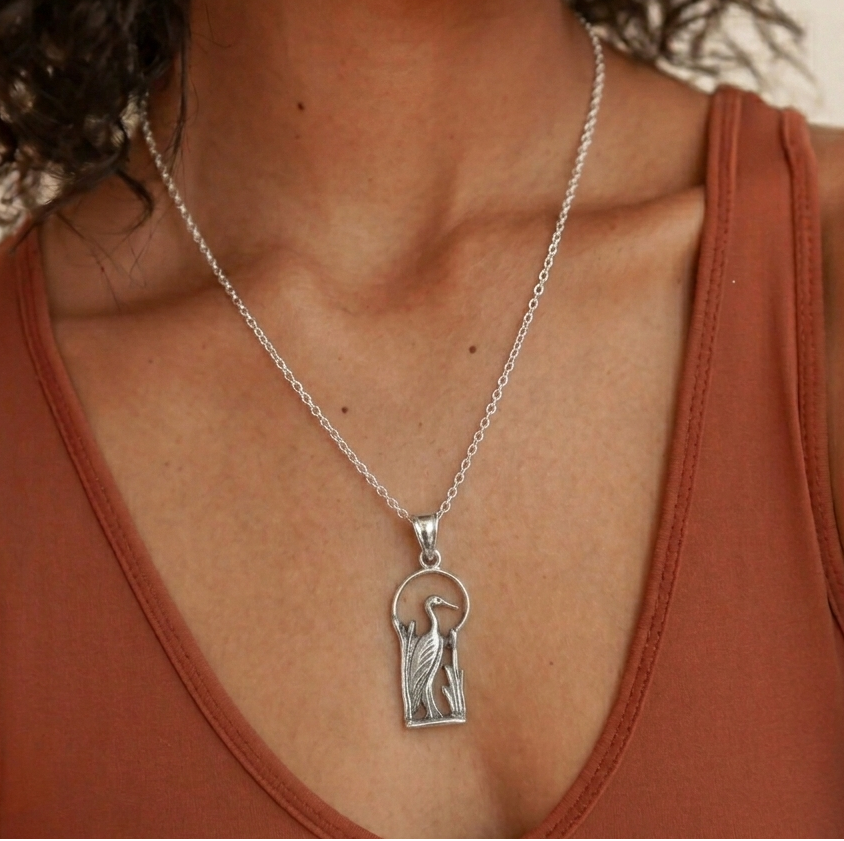 Silver necklace with a pendant worn by a person in a brown top.