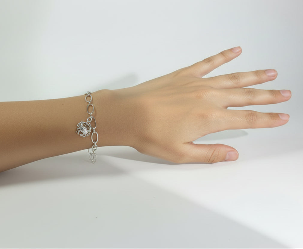 Silver bracelet with a crab charm on a wrist against a neutral background