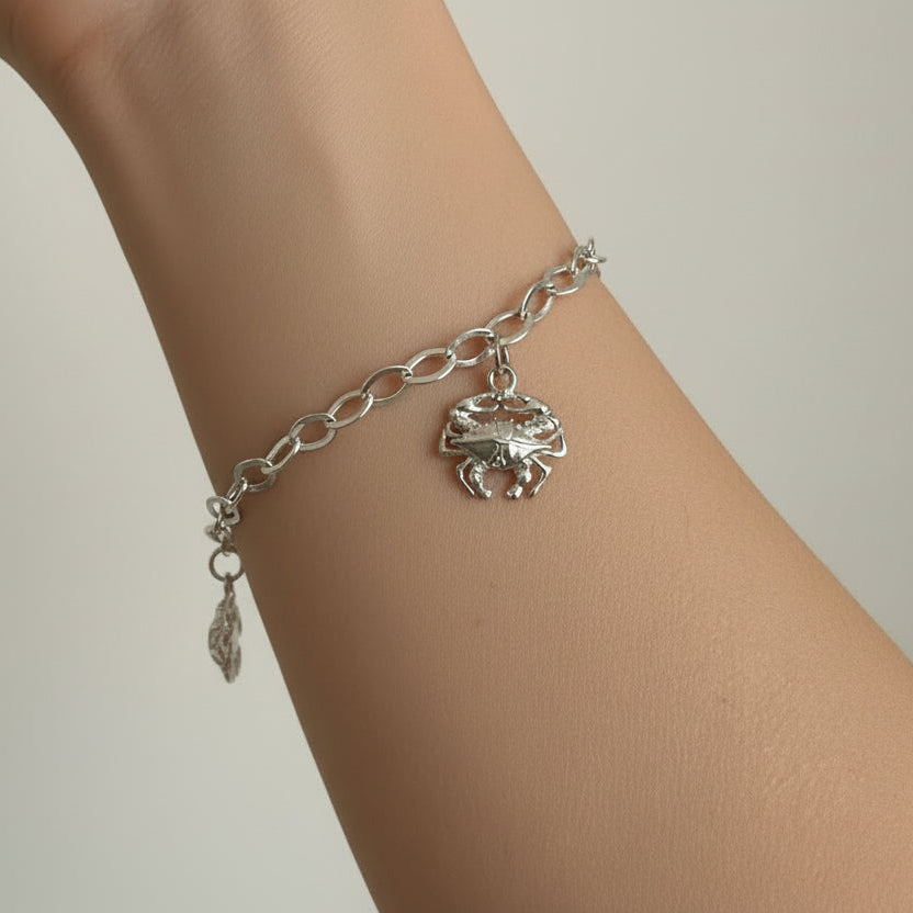 Silver chain bracelet with crab charm on a wrist against a neutral background