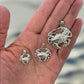 Three silver crab pendants on a hand with a blurred beach background