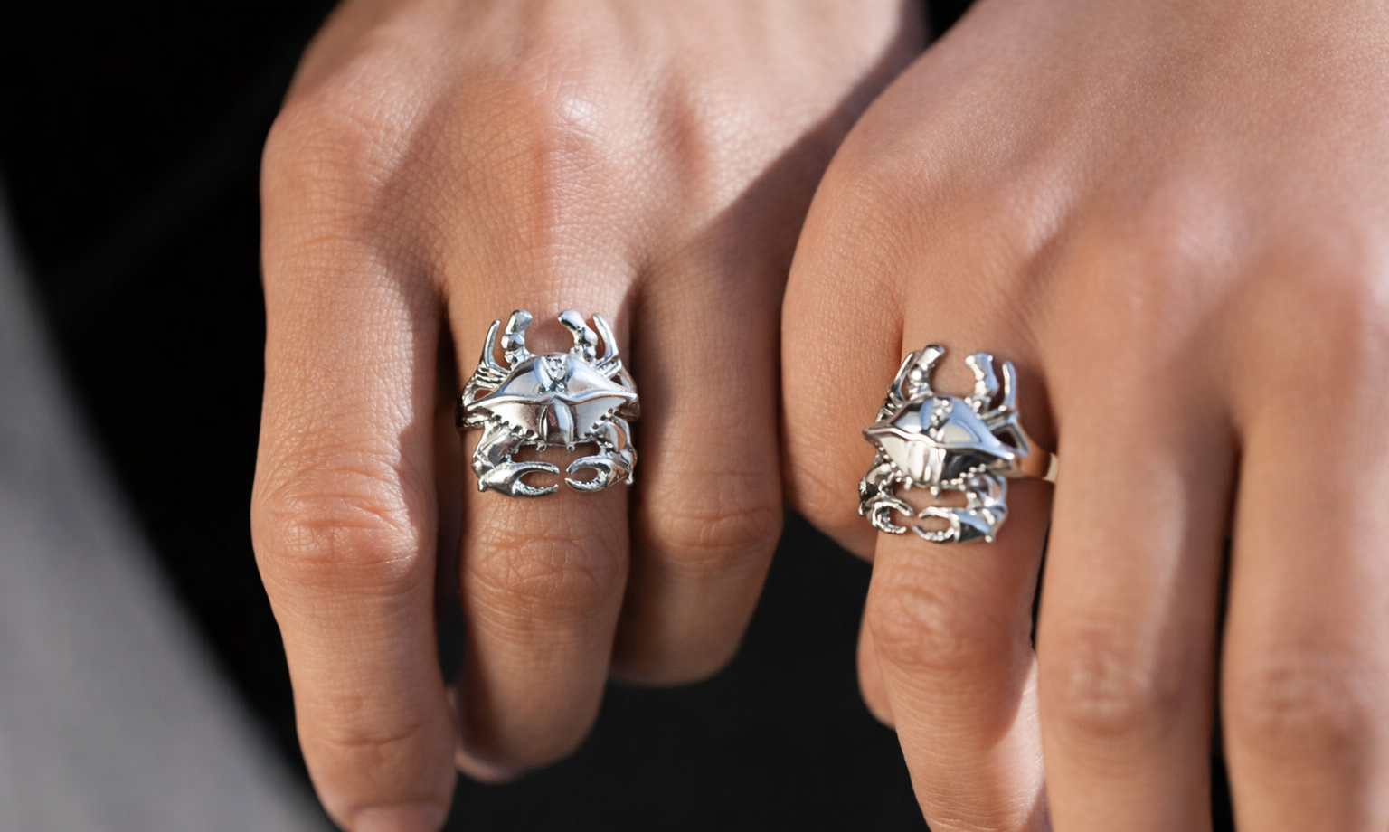 Close-up of two hands wearing silver rings with star designs on a neutral background
