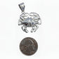 Silver crab pendant next to a quarter for scale on a white background