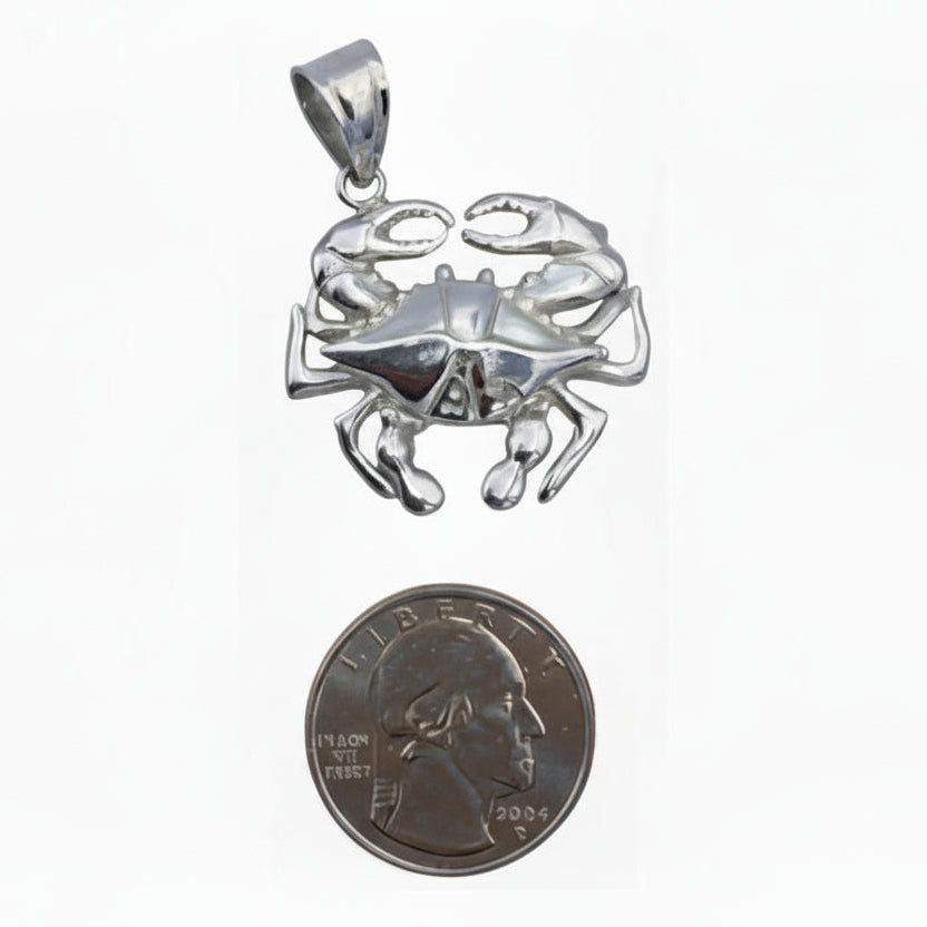 Silver crab pendant next to a quarter for scale on a white background