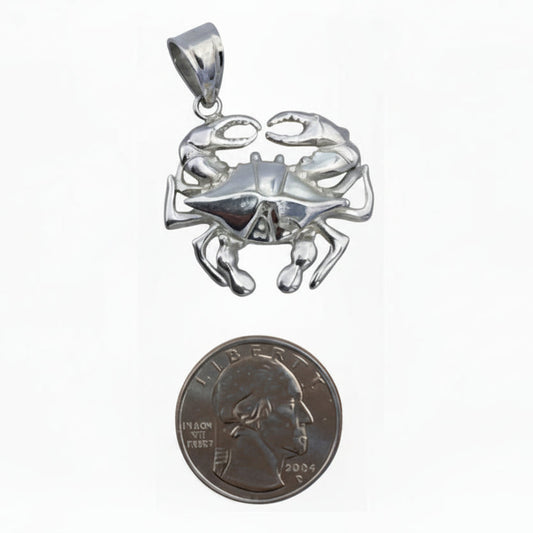 Silver crab pendant next to a quarter for scale on a white background