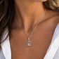 A woman wearing a silver-toned blue crab pendant necklace, styled with a white linen shirt against an outdoor lakeside background.
