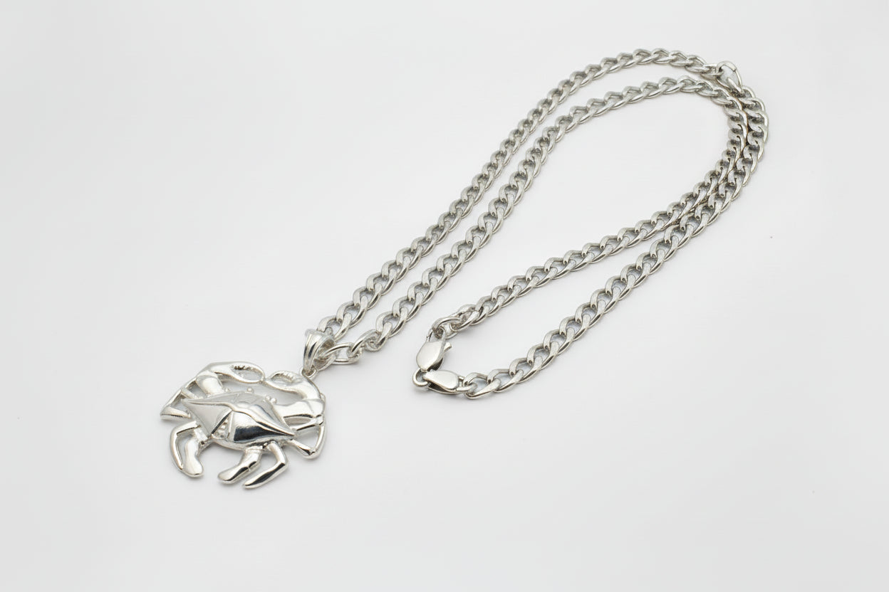 Silver chain necklace with a blue crab pendant on a gray background