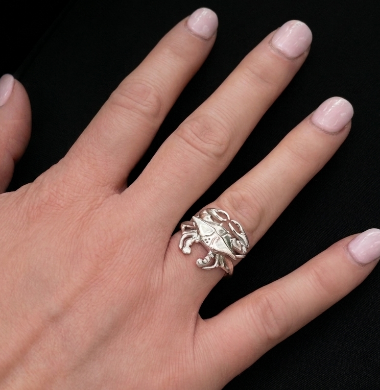 Hand wearing a silver crab-shaped ring on a black background