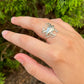 Hand wearing a silver blue crab ring  against a green foliage background