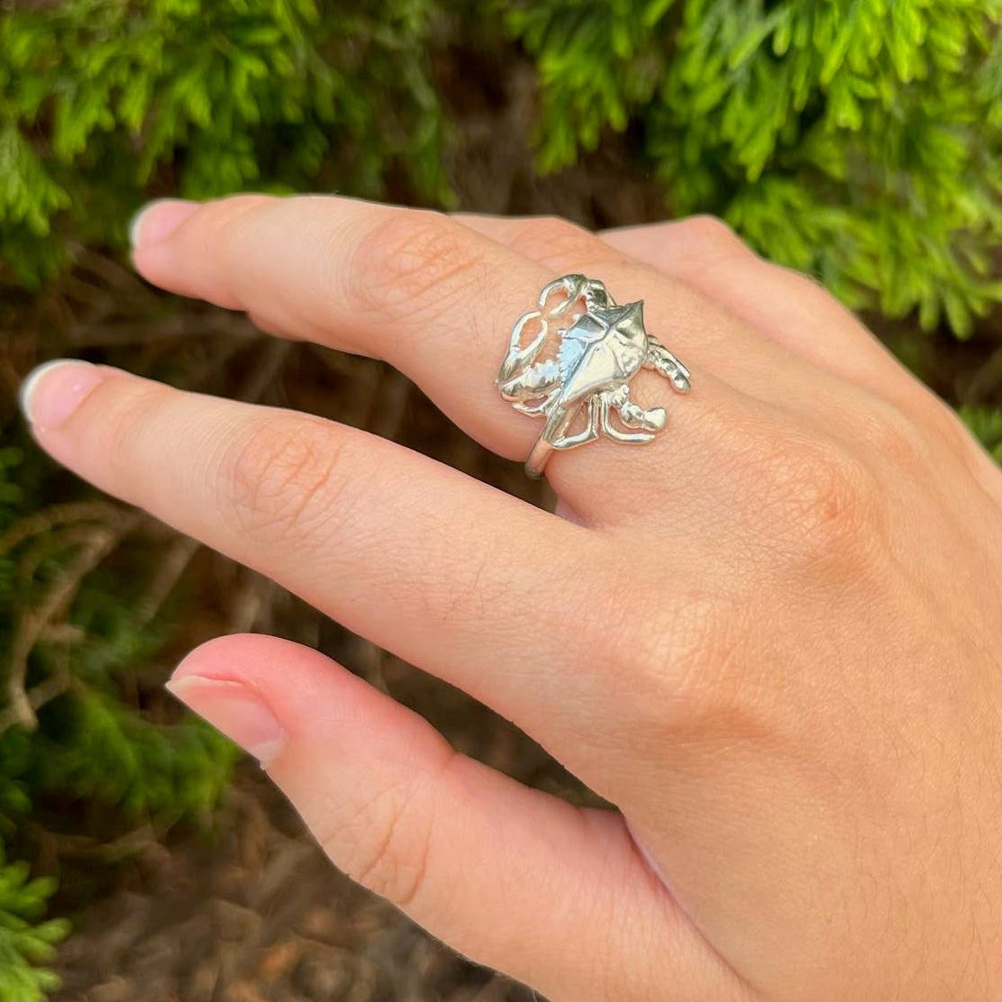 Hand wearing a silver blue crab ring  against a green foliage background