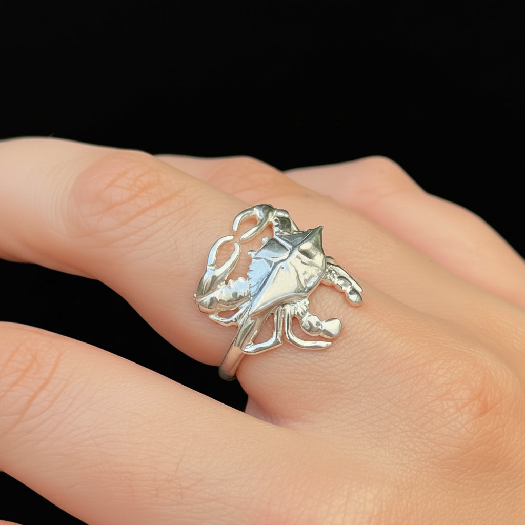 Hand wearing a silver blue crab ring  against a green foliage background
