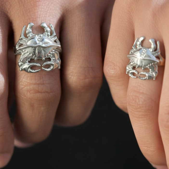 Two hands wearing silver crab-themed rings against a dark background