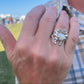 Hand wearing a silver blue crab ring outdoors on a sunny day.