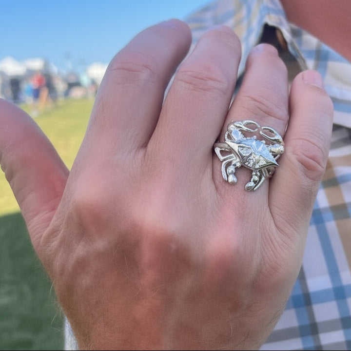 Hand wearing a silver blue crab ring outdoors on a sunny day.