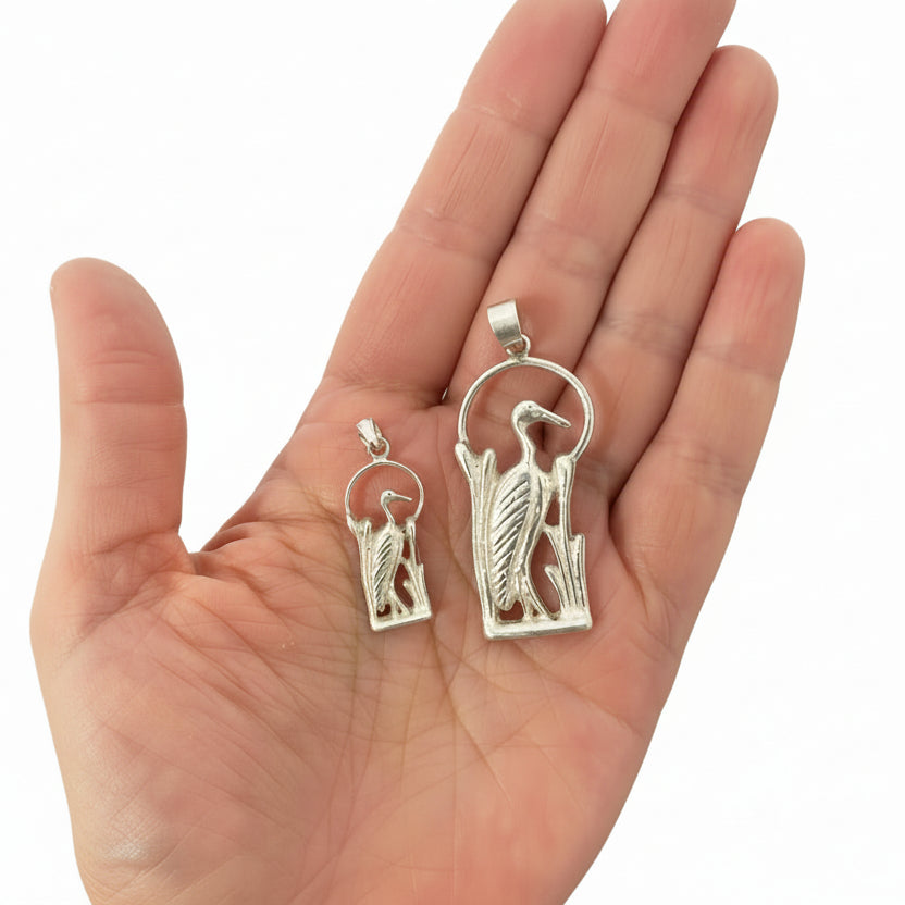 Hand holding two silver bird pendants against a white background