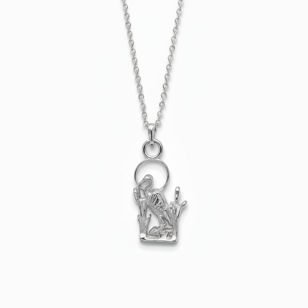 A sterling silver pendant featuring a detailed cutout design of a heron standing among reeds, complete with a circular ring at the top for a chain.
