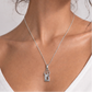 Woman wearing a silver necklace with a pendant against a plain background