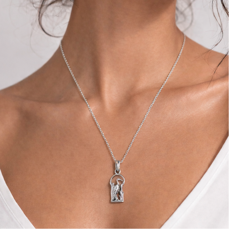 Woman wearing a silver necklace with a pendant against a plain background