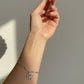 Hand wearing a silver bracelet with a starfish charm against a neutral background