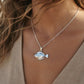 A woman wearing a silver fish pendant necklace, with the blue ocean and sky in the background.