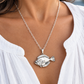 A silver fish pendant necklace worn by a model in a white blouse, featuring a detailed silver fish charm on a delicate chain.