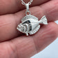 A silver fish pendant necklace held on a person's fingers against a light gray background.