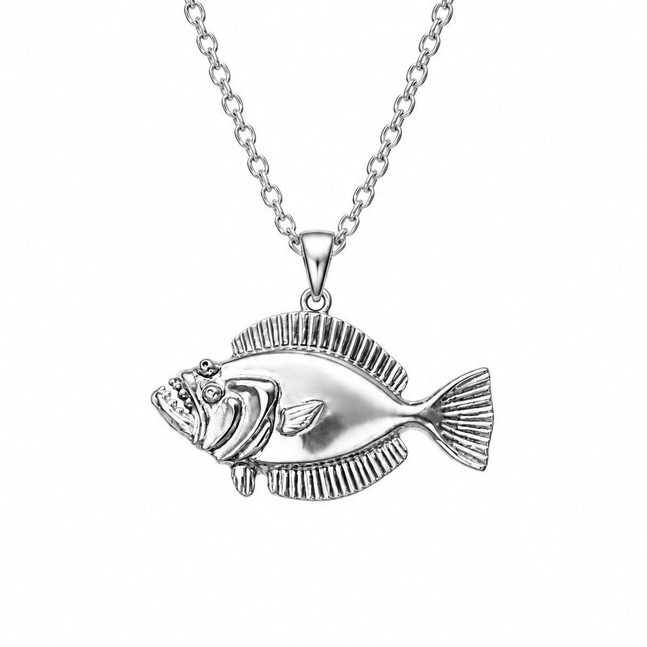 A silver fish pendant with detailed scales and a textured fin, held in a person's hand against a plain light background.