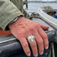 Hand with a silver ring on a boat railing by a body of water