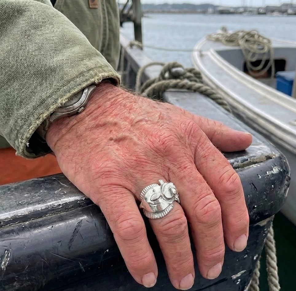 Hand with a silver ring on a boat railing by a body of water