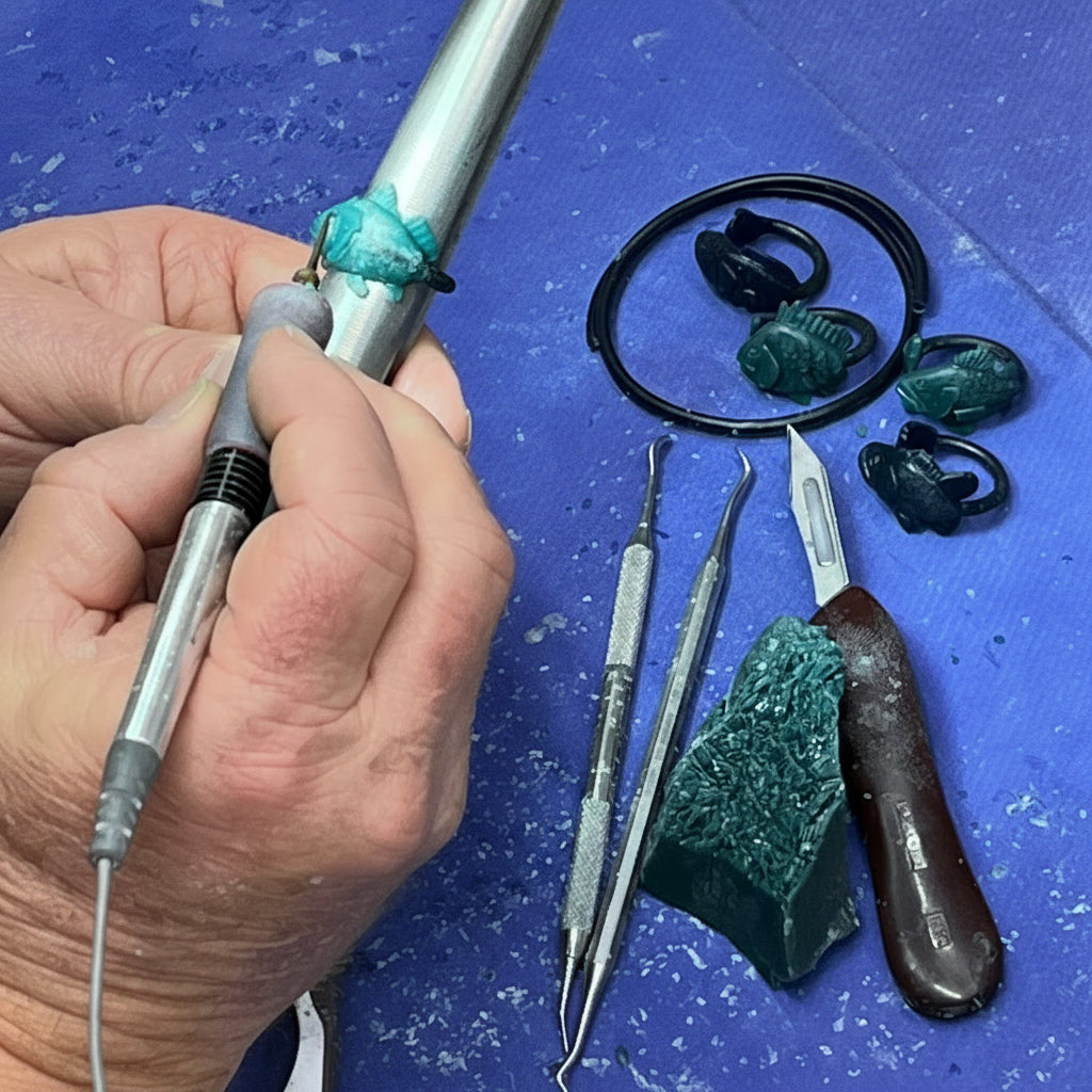 Hand holding dental tool with dental instruments showing process of lost wax technique using green wax to create fish rings on a blue surface