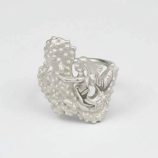 A silver ring featuring an octopus with a mermaid sitting on top, set against a textured background.