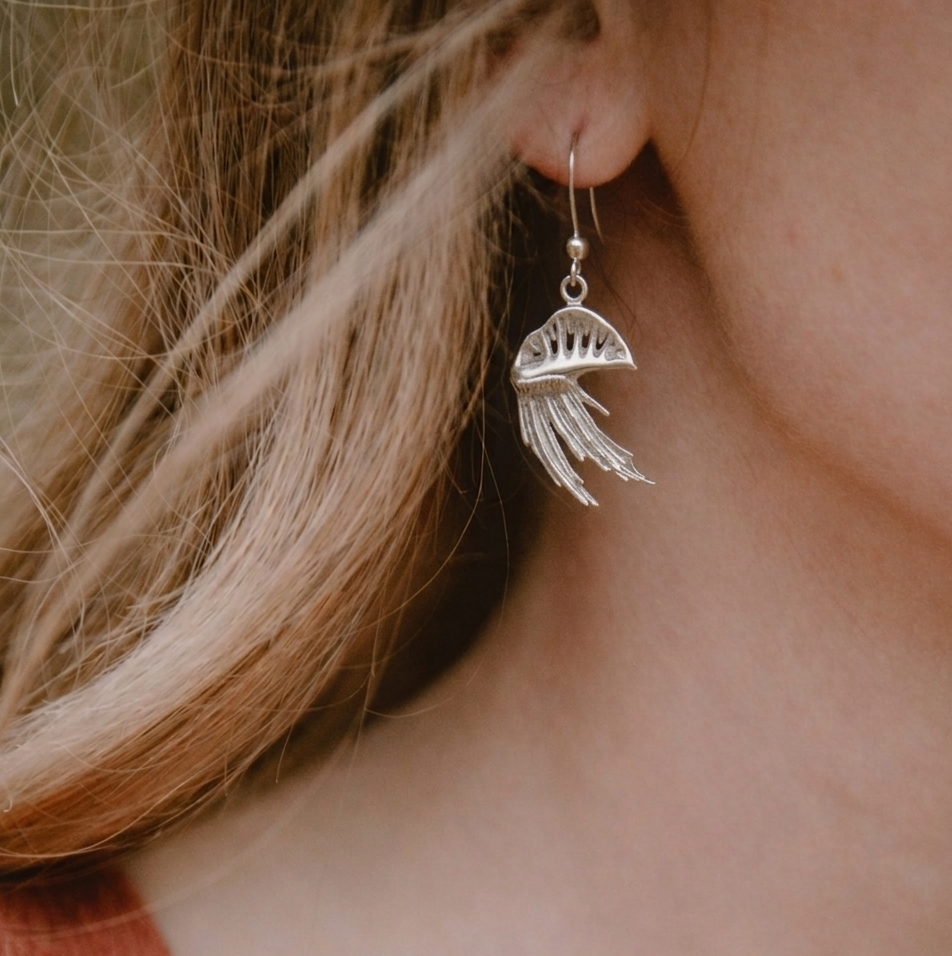 Silver man o' war earring worn by a person with blonde hair.
