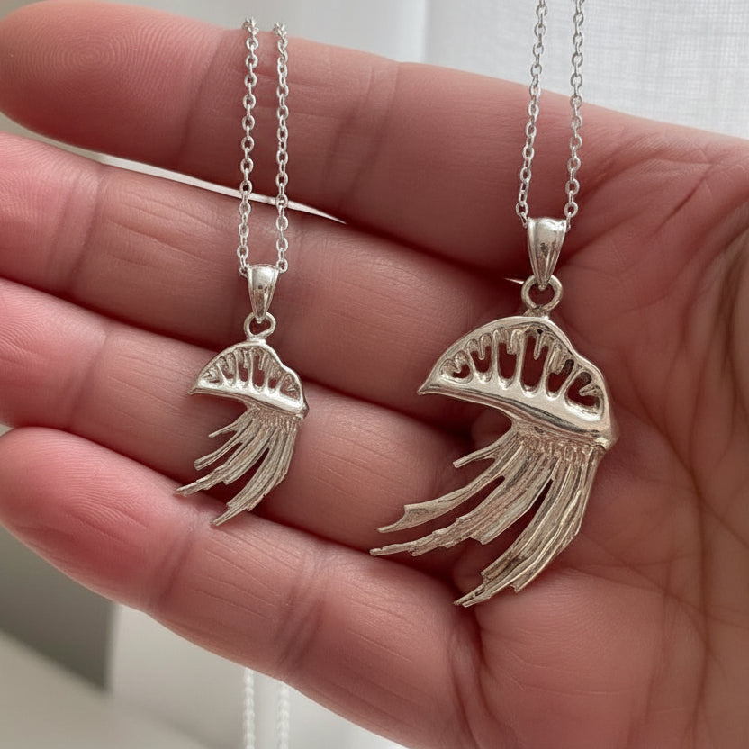Two silver man o' war-shaped pendants on chains held in a hand.
