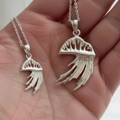 Hand holding two silver Portuguese man o' war pendants on chains against a neutral background