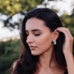 Woman wearing earrings outdoors with greenery in the background