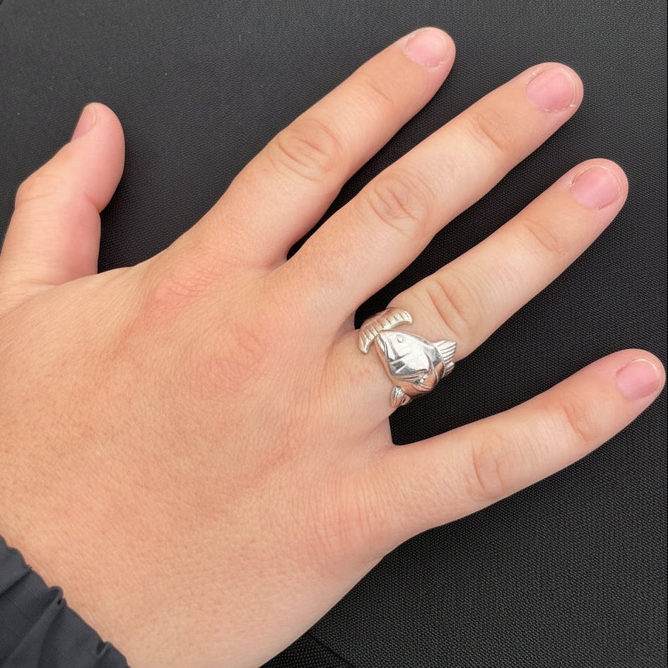 Hand wearing two silver rings on a dark surface