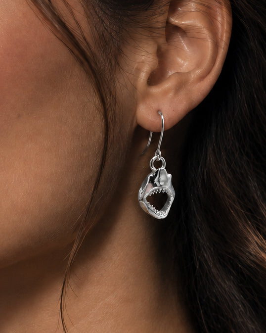 A pair of silver dangling earrings shaped like stylized shark mouth on lady model