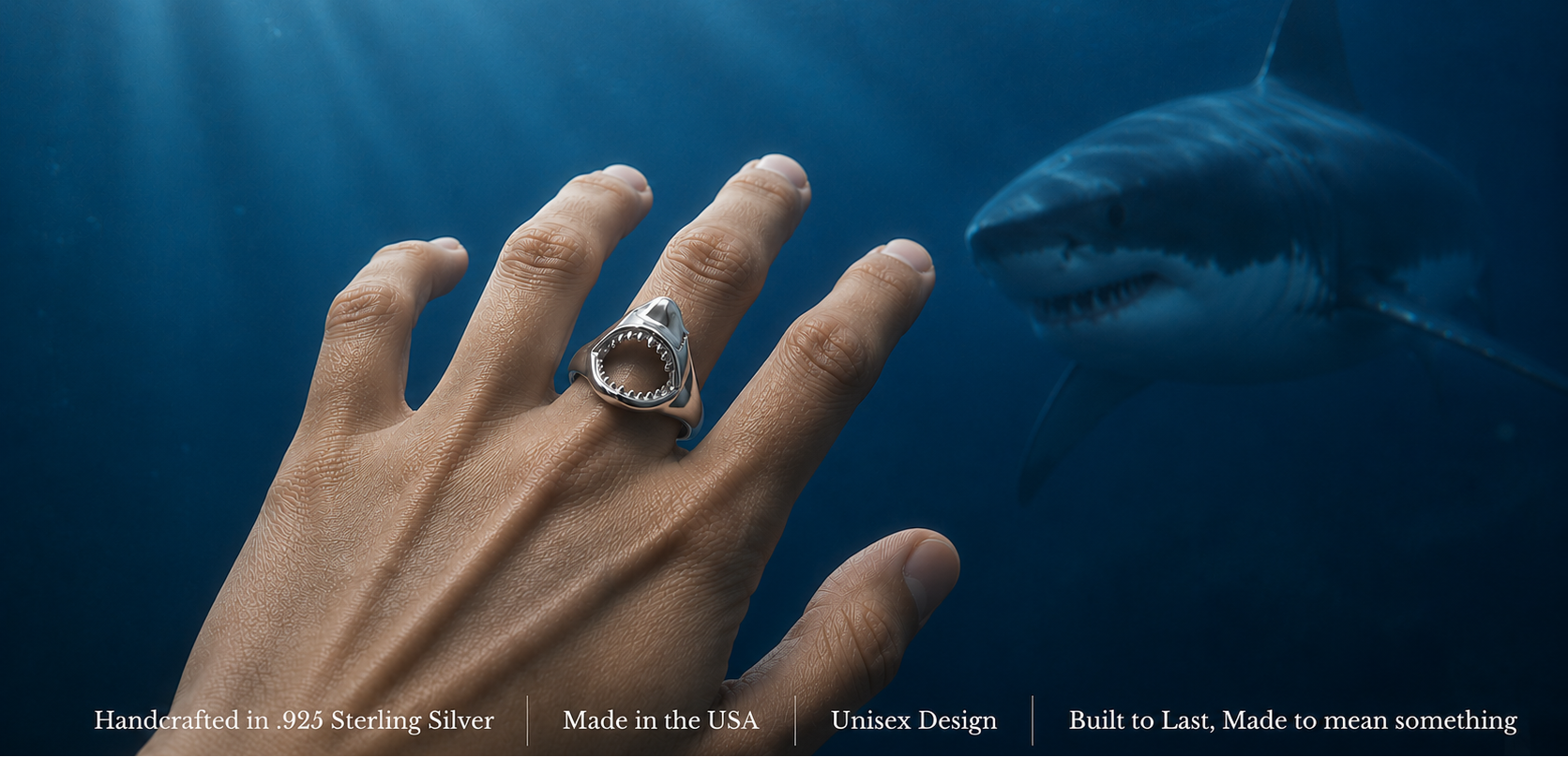 A hand wearing a silver shark-tooth ring, set against an underwater scene with a great white shark swimming in the blue water. Text at the bottom reads: 'Handcrafted in .