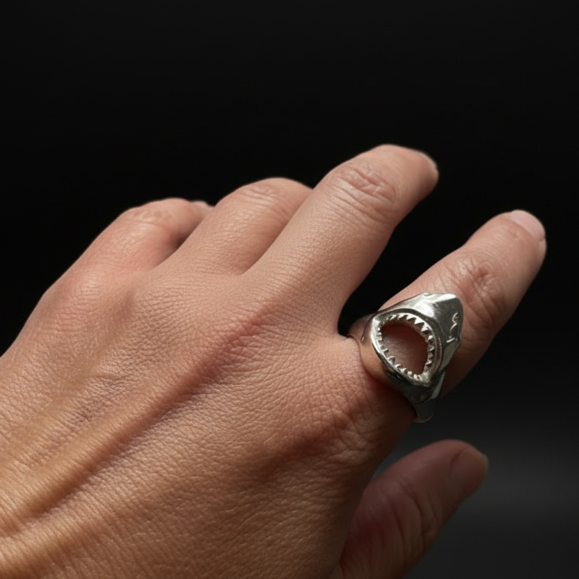 Hand wearing a silver shark ring on a black background