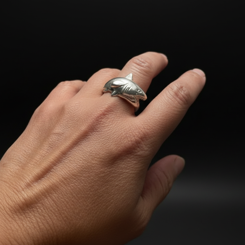 Hand wearing two silver shark tooth rings on a dark background