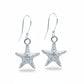A pair of silver starfish dangle earrings with textured starfish charms and silver fishhook wires, displayed on a light blue background.