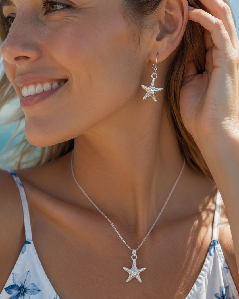 A close-up lifestyle shot of a woman wearing a silver starfish dangle earring, with her hand touching her hair against a bright, sunny outdoor background.