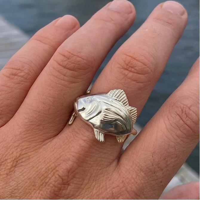 Hand wearing a silver fish-shaped ring with a marina background