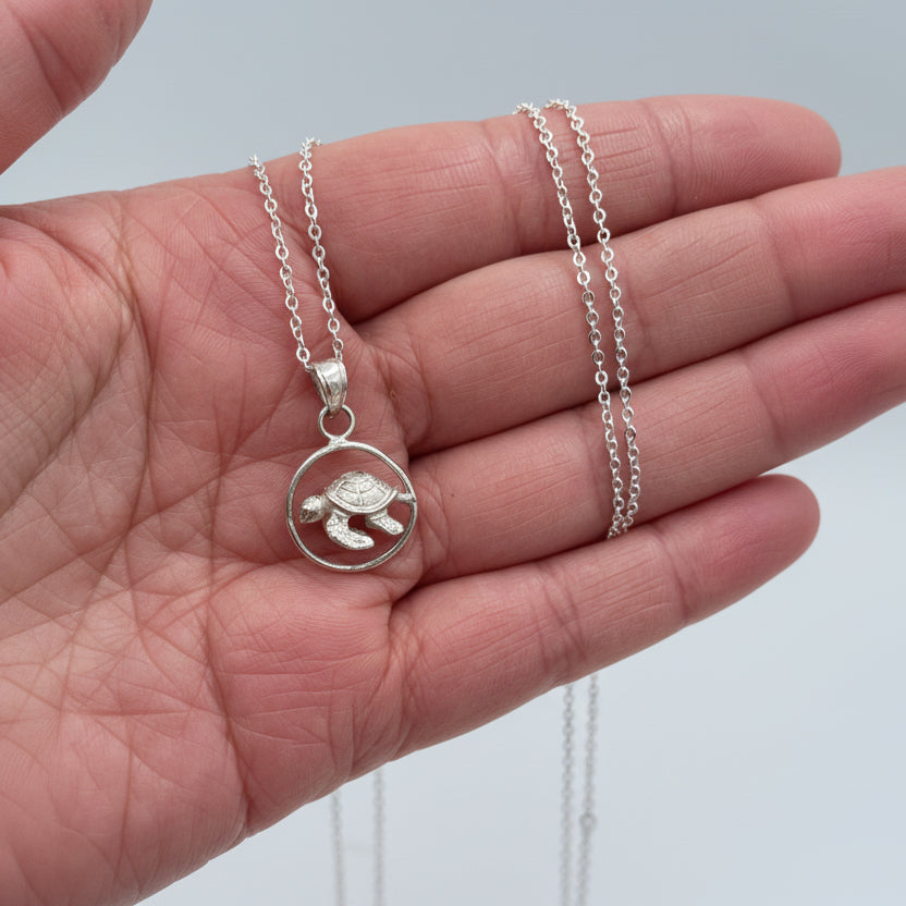 Turtle Necklace on hand on light gray background
