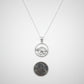 Silver necklace with a pendant next to a penny on a light gray background