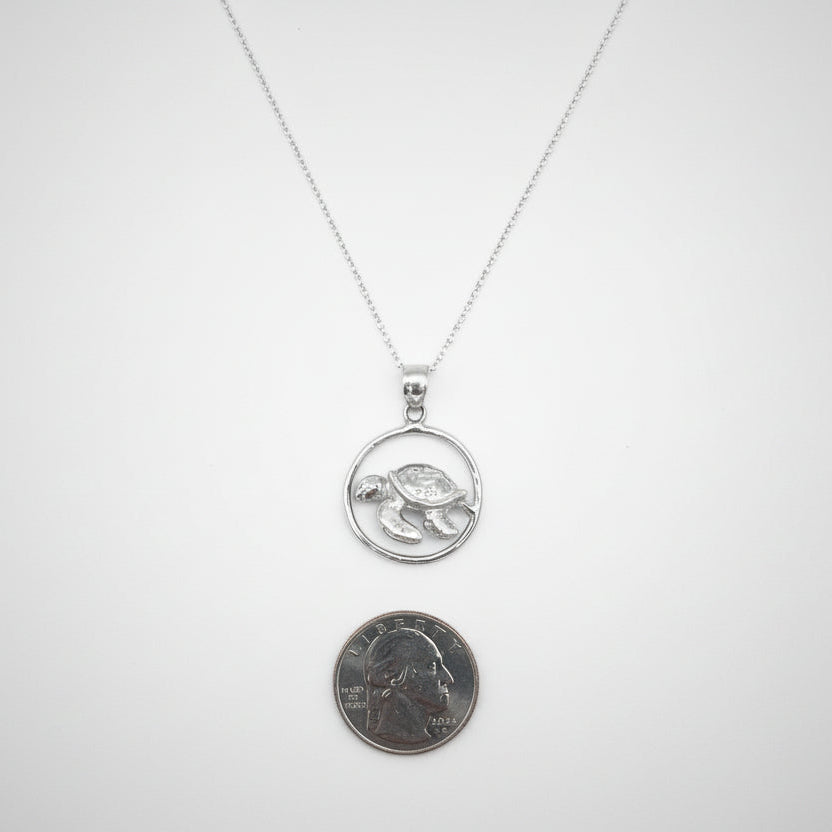 Silver necklace with a pendant next to a penny on a light gray background